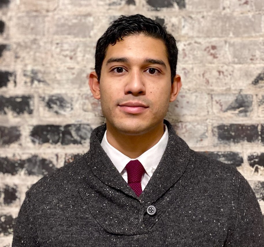 Portrait of Hispanic man with tie and white short covered with a sweater in front of a brick wall